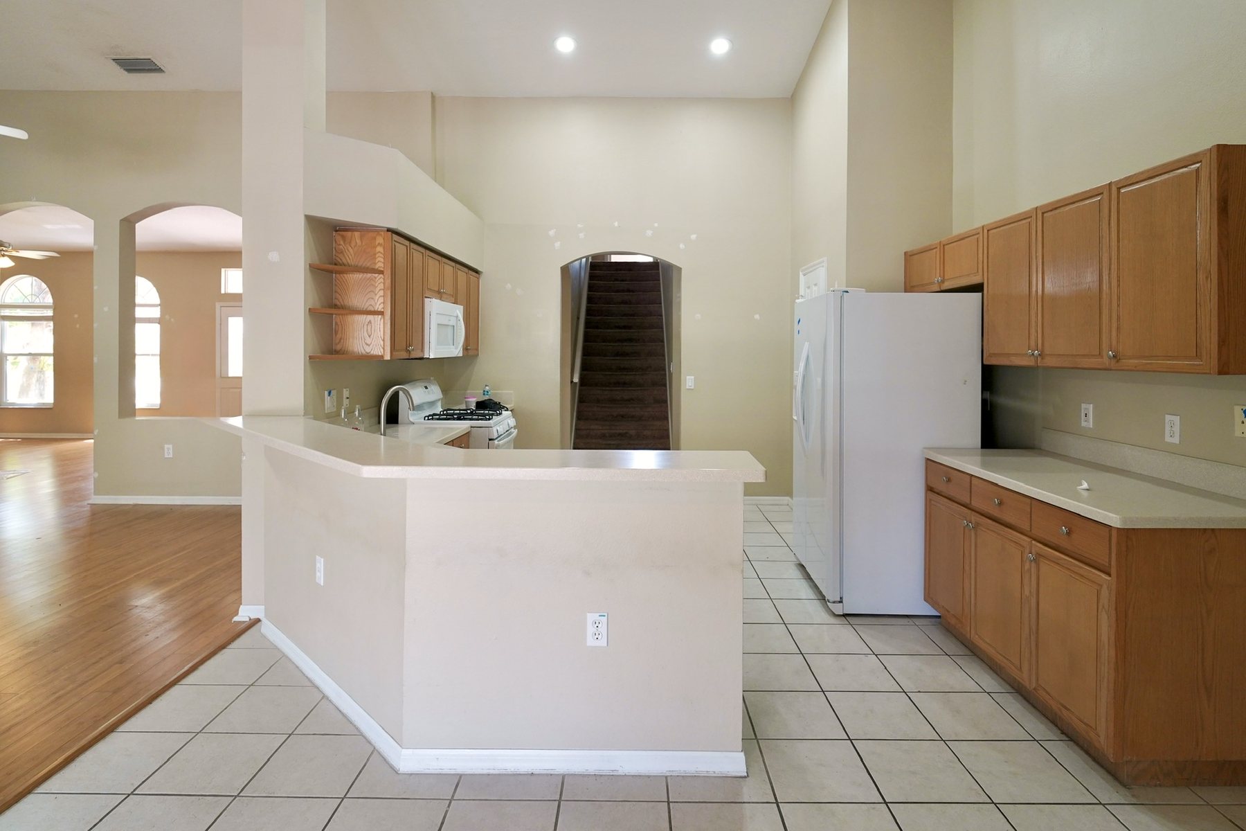 The kitchen before: dated oak cabinets, a raised peninsula and a white tile floor.