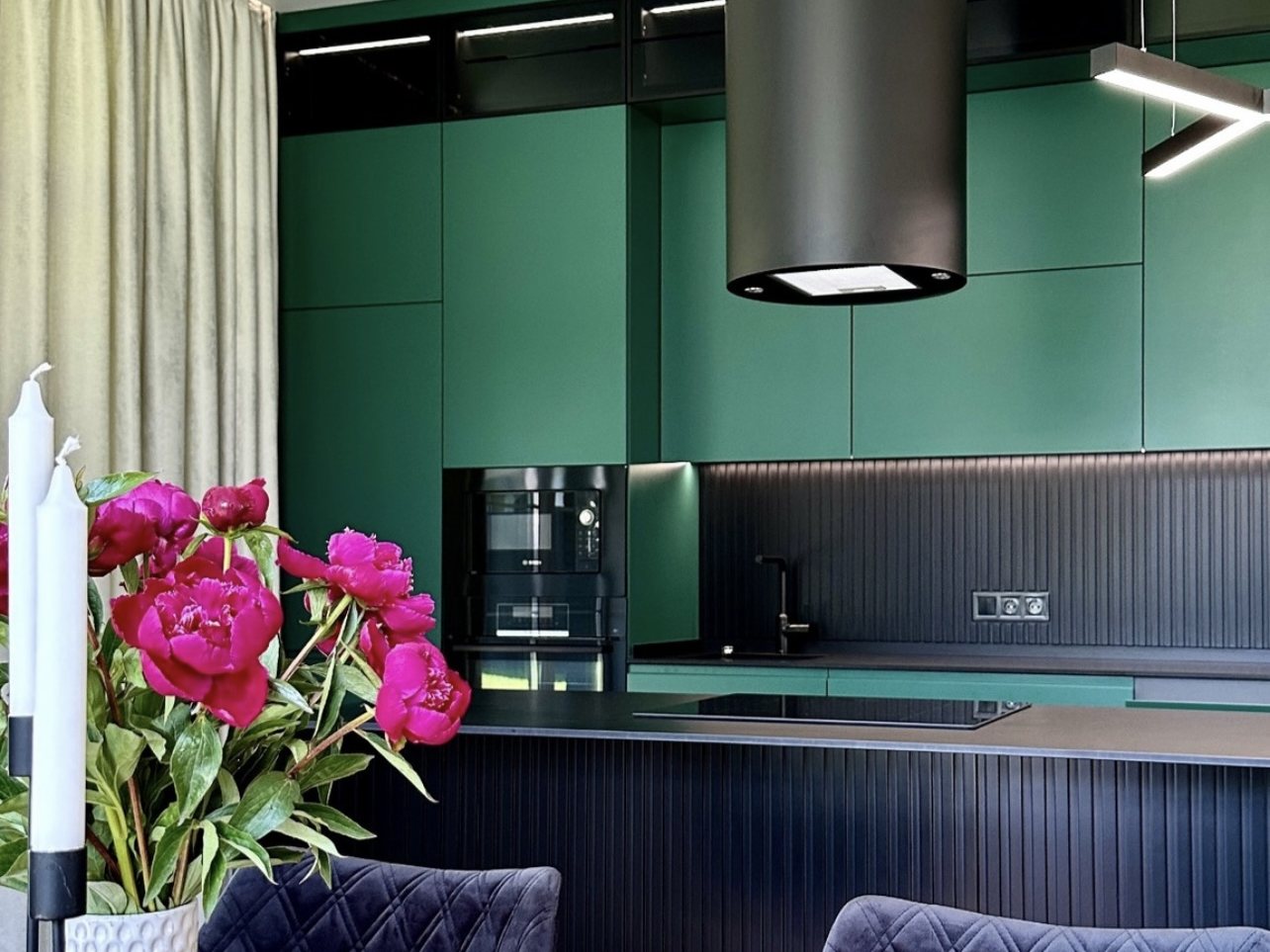 Green tall cabinetry with a built-in coffee machine and a black island with a fluted front.