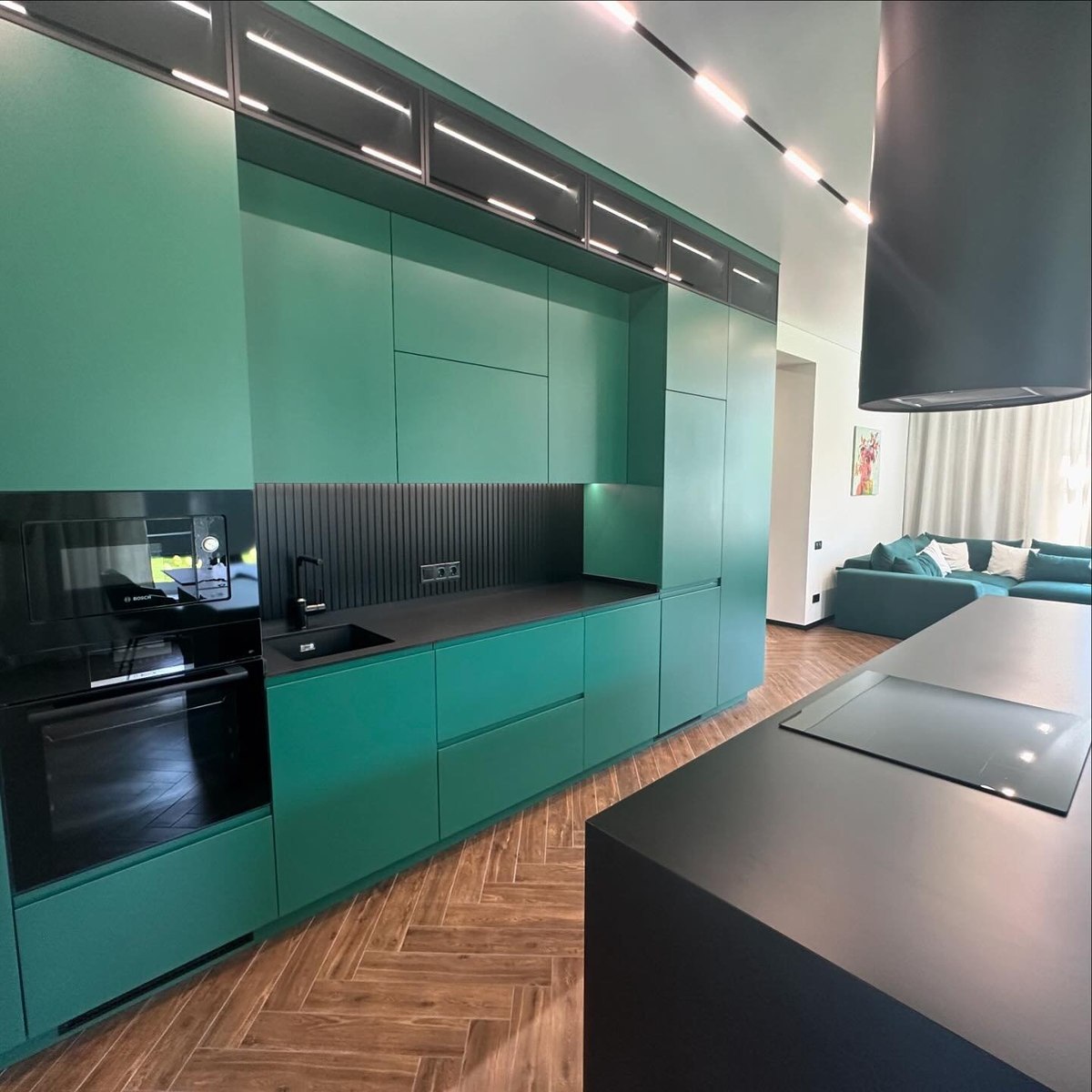 Full-height green flat-panel cabinetry with integrated appliances and a black island.
