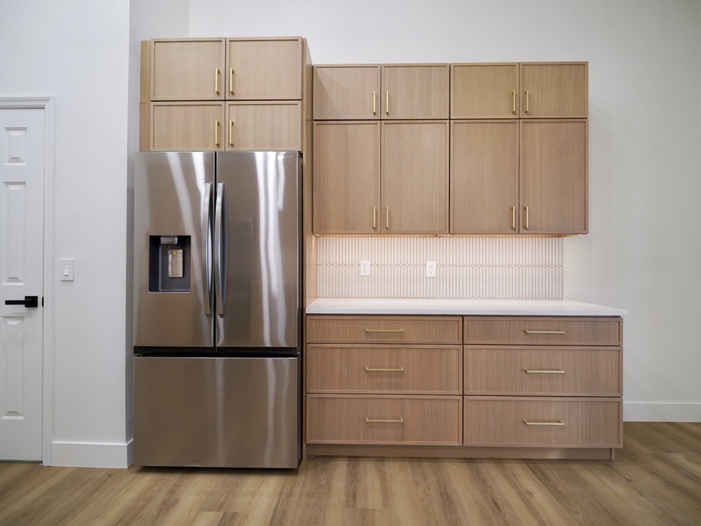 Light oak flat-panel cabinets around a stainless refrigerator, with brass bar pulls.