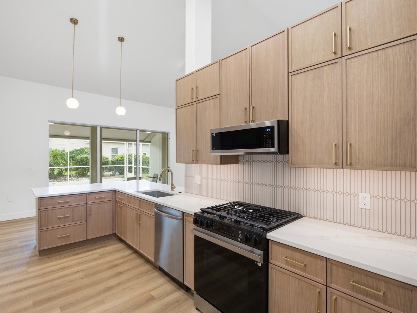 Finished kitchen with light oak flat-panel cabinets, brass pulls, a white quartz countertop and a cream picket-tile backsplash behind a gas range.