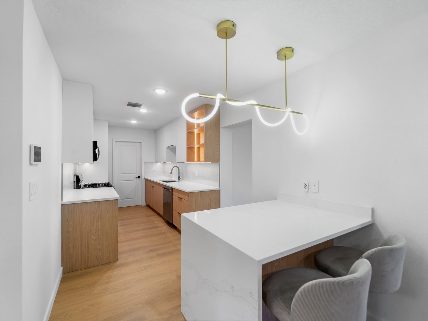 White upper cabinets over oak lowers, with a white quartz waterfall island and banquette seating.